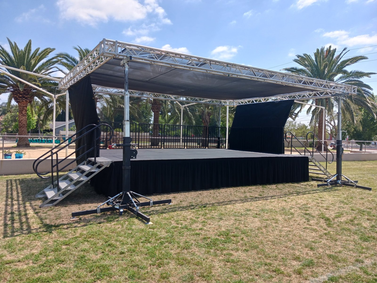 24 x 16 x 3 Steeldeck stage rental with shade roof, aluminum stairs, safety railing, and black stage skirting